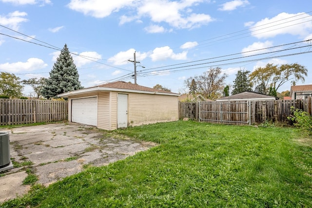 view of yard with driveway, a fenced backyard, a detached garage, and an outdoor structure