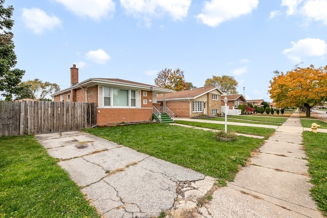 view of front facade with a front yard, a chimney, fence, and brick siding