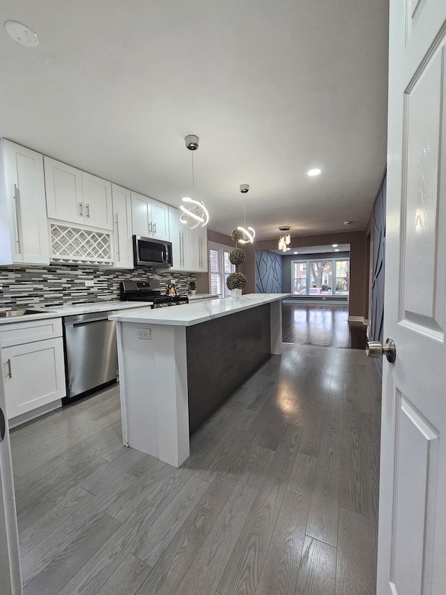 kitchen featuring stainless steel appliances, wood finished floors, open floor plan, light countertops, and backsplash