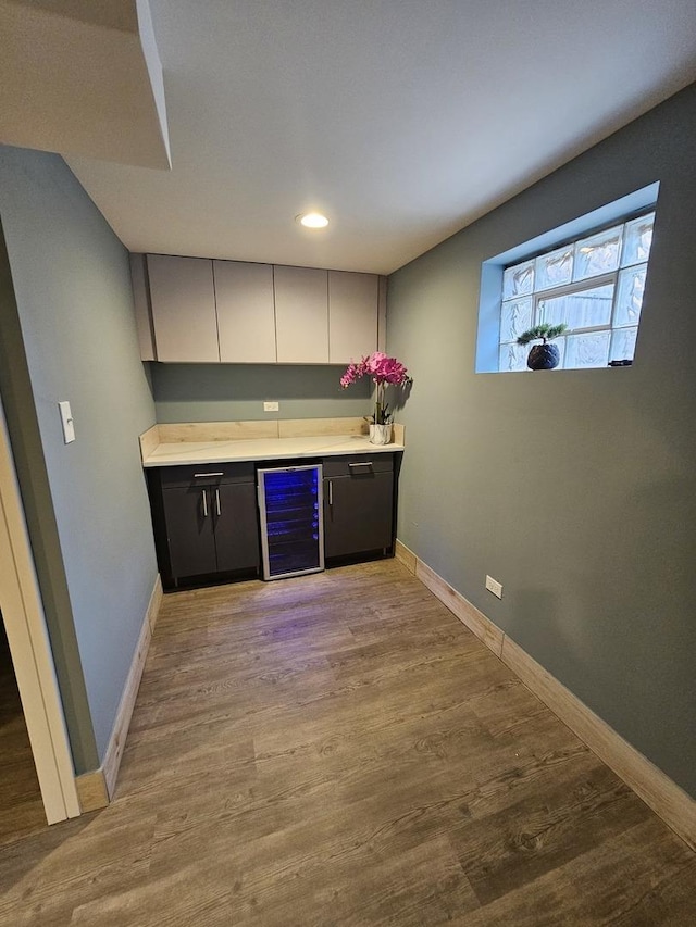 bar featuring a bar, wine cooler, baseboards, and wood finished floors