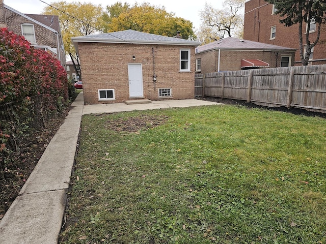 rear view of property featuring brick siding, a yard, entry steps, a patio area, and fence private yard