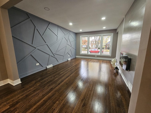 unfurnished living room with baseboards, visible vents, dark wood finished floors, a decorative wall, and recessed lighting