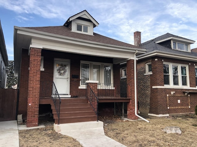 bungalow-style house with roof with shingles, a porch, and brick siding