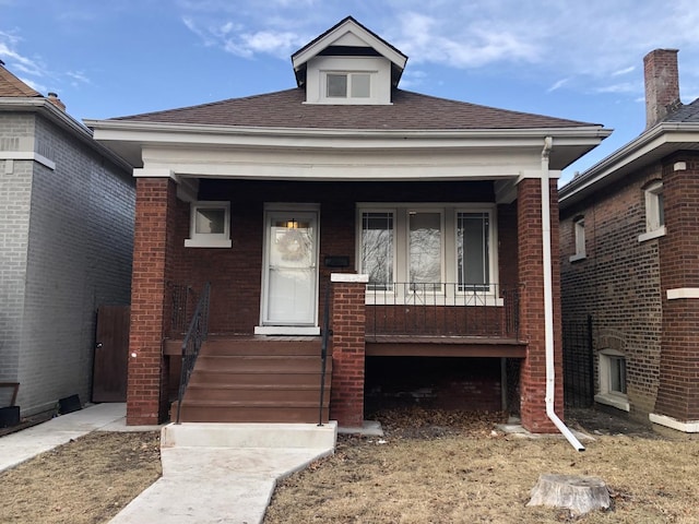 view of front of home with covered porch, roof with shingles, and brick siding