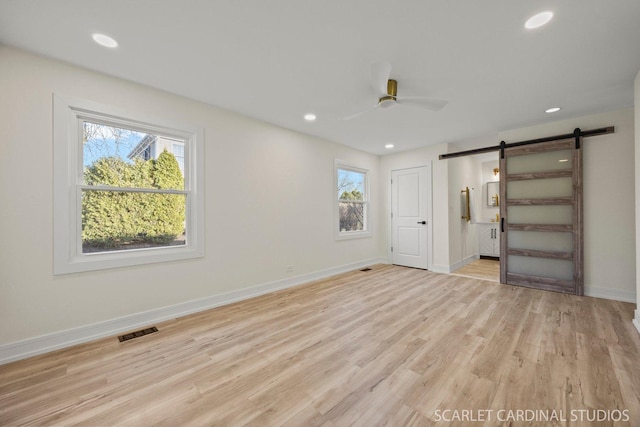 unfurnished bedroom with visible vents, light wood finished floors, multiple windows, and a barn door