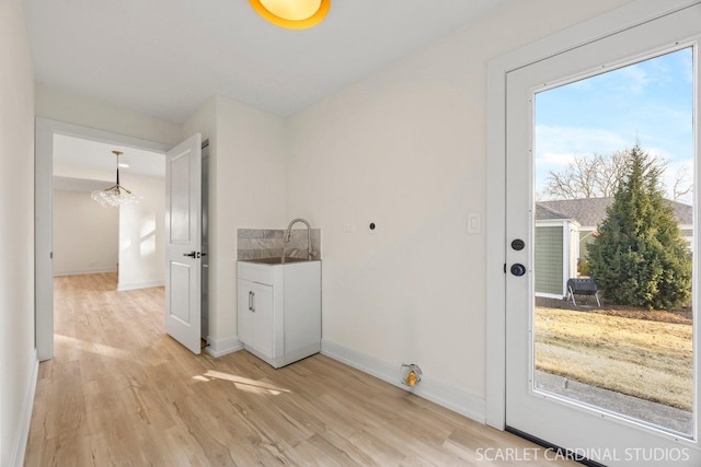 clothes washing area with hookup for an electric dryer, a sink, baseboards, light wood-style floors, and cabinet space