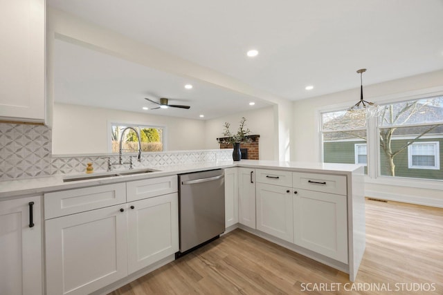 kitchen with light countertops, light wood-style flooring, decorative backsplash, a sink, and dishwasher