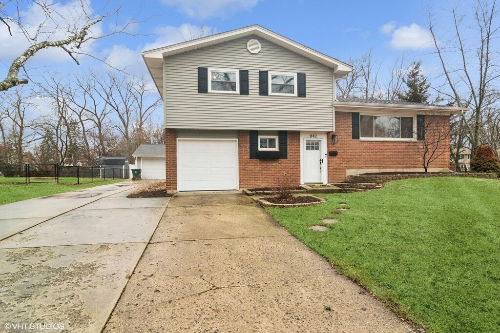 tri-level home with a garage, brick siding, fence, concrete driveway, and a front lawn