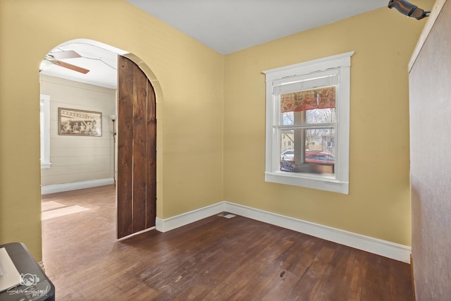 spare room with arched walkways, ceiling fan, wood-type flooring, and baseboards