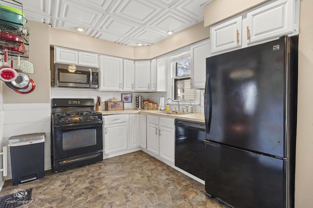 kitchen with an ornate ceiling, light countertops, black appliances, white cabinetry, and a sink