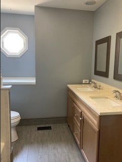 bathroom with double vanity, a sink, toilet, and wood finished floors