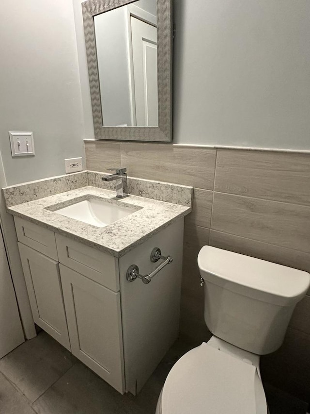 bathroom with vanity, tile walls, toilet, and a wainscoted wall