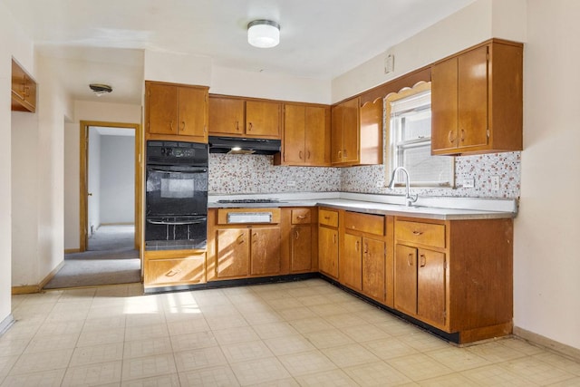 kitchen with tasteful backsplash, light countertops, brown cabinetry, a sink, and under cabinet range hood