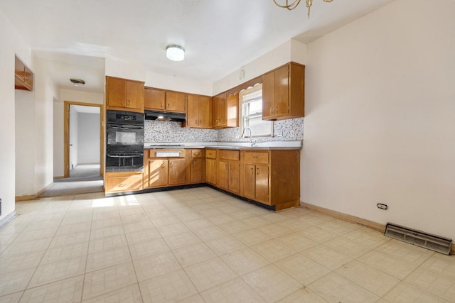 kitchen with decorative backsplash, brown cabinetry, light floors, light countertops, and under cabinet range hood