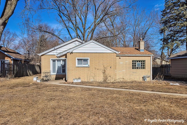 rear view of property with a chimney, fence, and brick siding