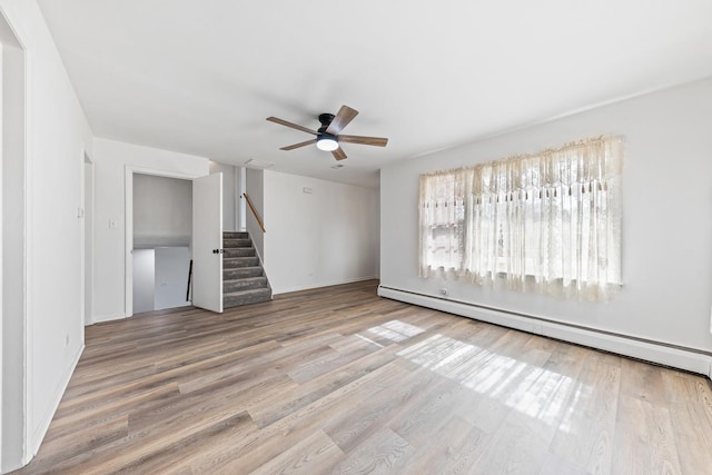 empty room featuring a ceiling fan, wood finished floors, baseboard heating, and stairs