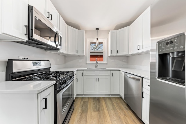 kitchen featuring light wood-style flooring, stainless steel appliances, light countertops, white cabinetry, and a sink