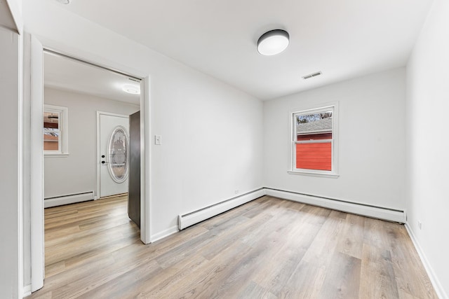 unfurnished room with a baseboard heating unit, visible vents, baseboards, and wood finished floors