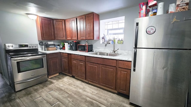 kitchen featuring stainless steel appliances, a sink, light countertops, and light wood-style floors