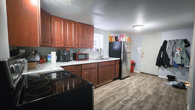 kitchen featuring light countertops, black electric range oven, light wood-style floors, freestanding refrigerator, and a sink