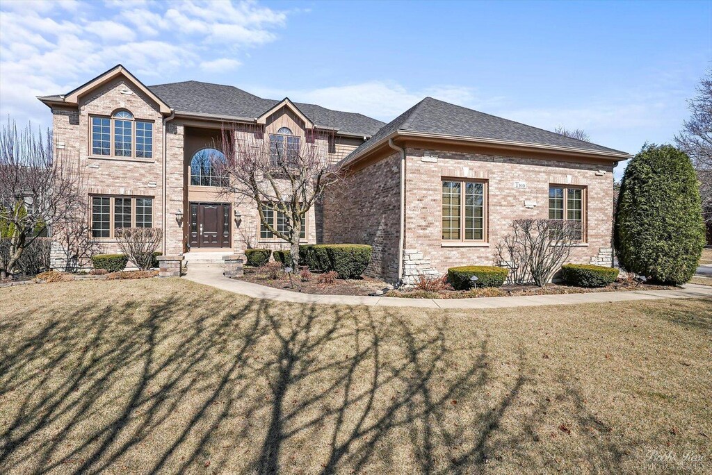 view of front of home with a shingled roof, a front lawn, and brick siding