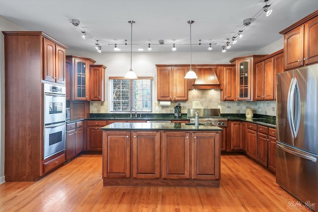 kitchen with a center island with sink, premium range hood, light wood-style flooring, a sink, and appliances with stainless steel finishes