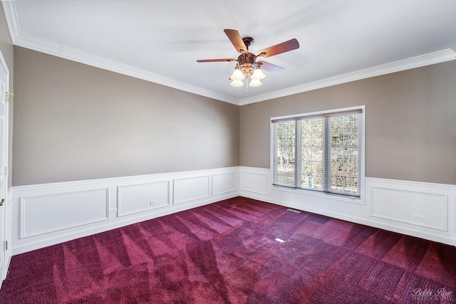 unfurnished room featuring a ceiling fan, a wainscoted wall, visible vents, ornamental molding, and dark colored carpet