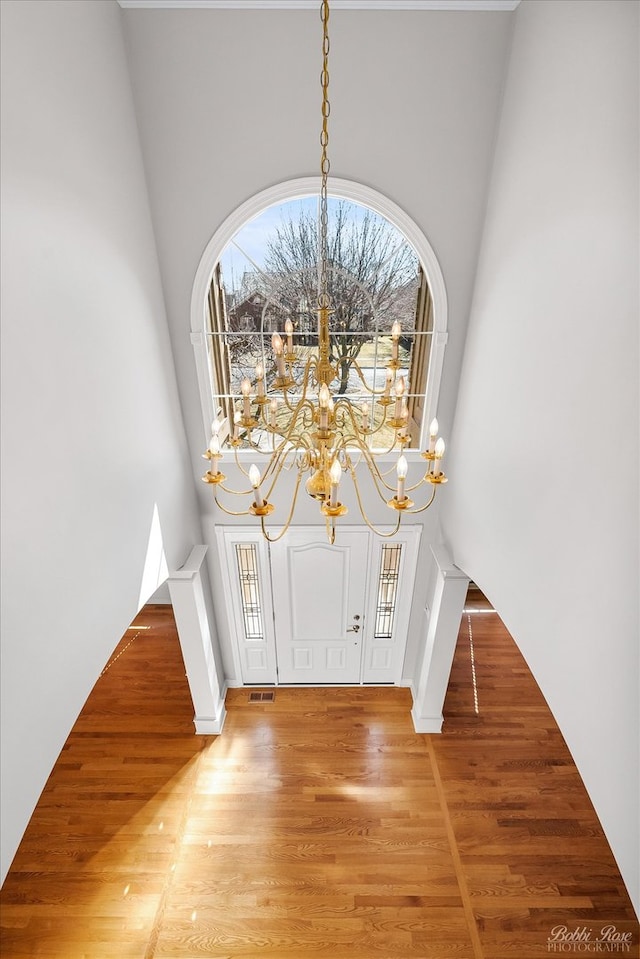 foyer with a notable chandelier, light wood-style flooring, visible vents, and a towering ceiling