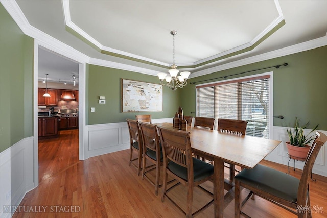 dining space featuring a raised ceiling, an inviting chandelier, wood finished floors, and wainscoting