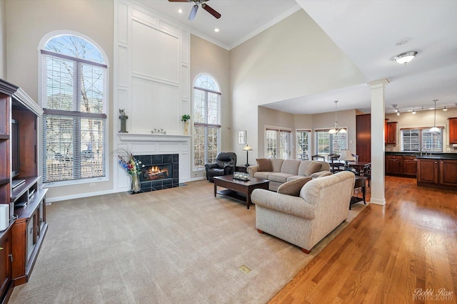 living room featuring a tiled fireplace, ornamental molding, a towering ceiling, and ceiling fan