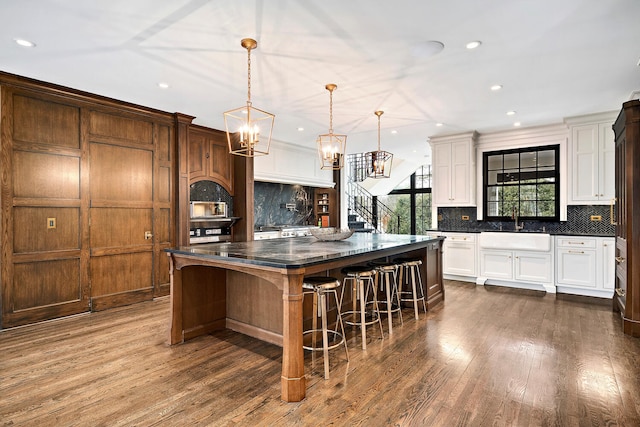 kitchen with dark countertops, a sink, backsplash, a kitchen breakfast bar, and dark wood-style flooring