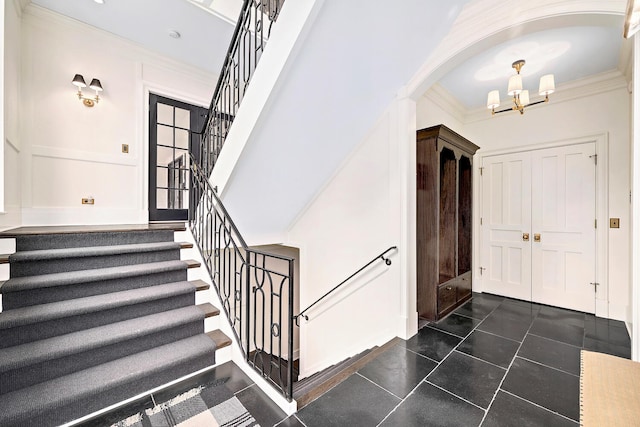 foyer entrance featuring crown molding, a chandelier, stairway, arched walkways, and dark tile patterned flooring