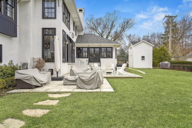 exterior space with roof with shingles, stucco siding, a yard, a sunroom, and a patio area