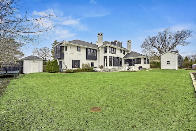 rear view of property featuring a chimney, a yard, a sunroom, an outbuilding, and a storage unit