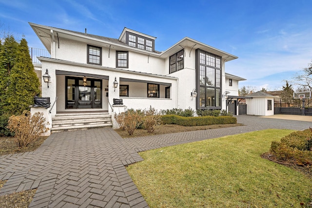 view of front of house featuring stucco siding, a front yard, driveway, and french doors