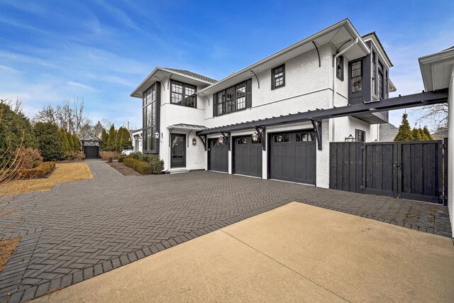 view of front of house with a gate, decorative driveway, an attached garage, and stucco siding