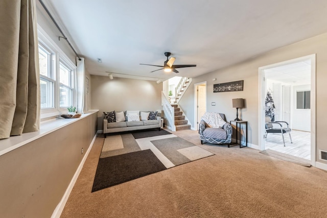 living room featuring visible vents, ceiling fan, baseboards, carpet, and stairs