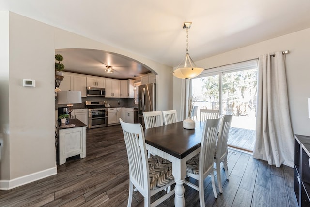 dining space with baseboards, arched walkways, and dark wood finished floors