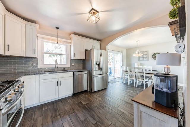 kitchen featuring dark wood-type flooring, decorative backsplash, arched walkways, stainless steel appliances, and a sink