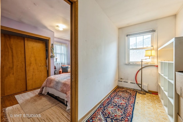 bedroom featuring a baseboard heating unit, wood finished floors, and baseboards