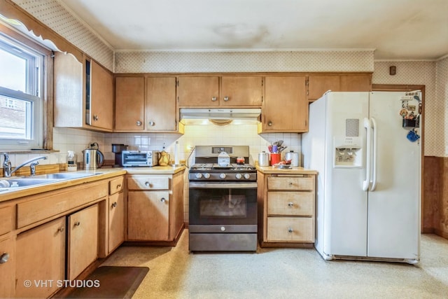 kitchen featuring wallpapered walls, under cabinet range hood, stainless steel range with gas stovetop, light floors, and white refrigerator with ice dispenser