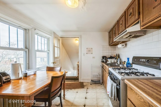 kitchen featuring brown cabinets, a sink, backsplash, baseboards, and white range with gas stovetop