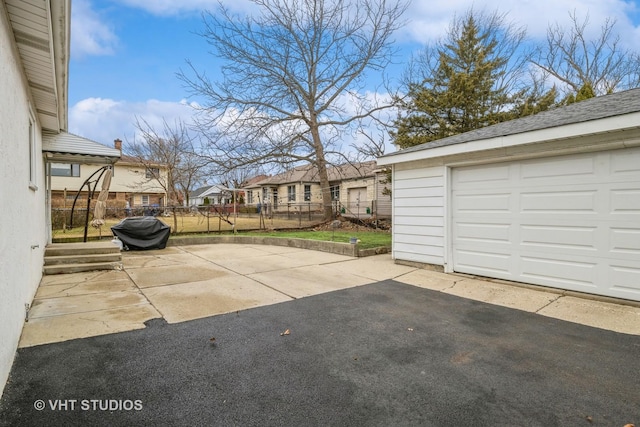 view of patio / terrace with an outbuilding, fence, a garage, aphalt driveway, and a residential view