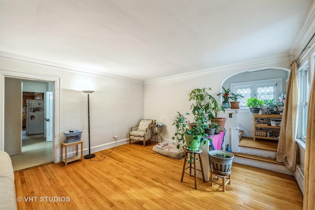 living area with arched walkways, crown molding, baseboards, and hardwood / wood-style flooring