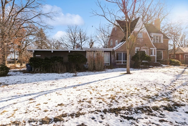 snow covered back of property with brick siding and a chimney