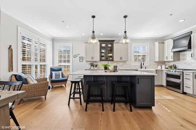 kitchen with light wood-style flooring, premium range hood, light countertops, double oven range, and a kitchen bar