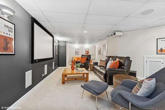 carpeted cinema room with a paneled ceiling and baseboards