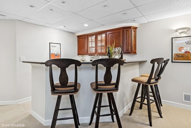 kitchen featuring light carpet, baseboards, glass insert cabinets, a kitchen breakfast bar, and a paneled ceiling