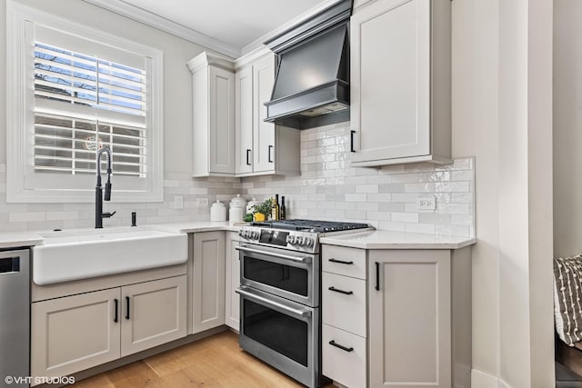 kitchen featuring premium range hood, a sink, appliances with stainless steel finishes, decorative backsplash, and light wood finished floors