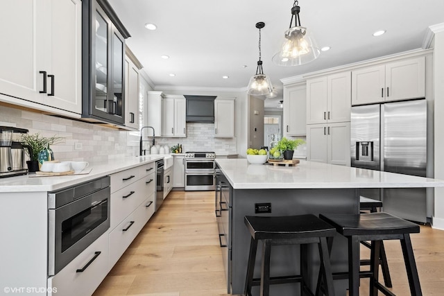 kitchen featuring stainless steel appliances, a kitchen island, light wood-style floors, ornamental molding, and a kitchen bar